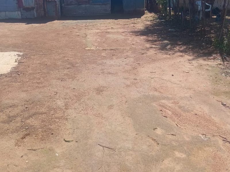 Front view of a residential property featuring corrugated metal structures and an unpaved yard area.
