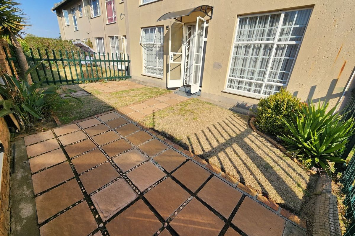 A private rear garden area featuring a paved patio, security gate, and metal fencing, providing direct access to the apartment.