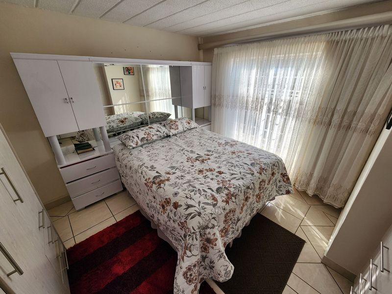 A bedroom featuring tiled flooring, a built-in wardrobe with integrated mirror, and a sliding glass door with curtains providing natural light.