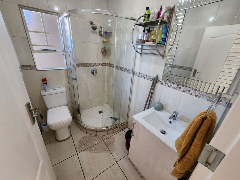 Compact bathroom featuring a corner shower enclosure, vanity basin, and toilet with neutral wall and floor tiling.