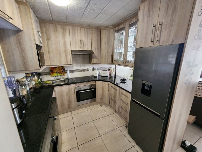 A well-maintained kitchen featuring light wood-grain cabinetry, black granite countertops, built-in oven, electric hob, and tiled flooring.