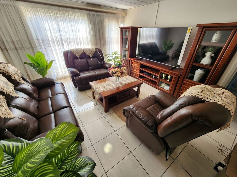 A comfortable living room featuring neutral tiled flooring and large windows with sheer curtains, providing a bright and functional space.
