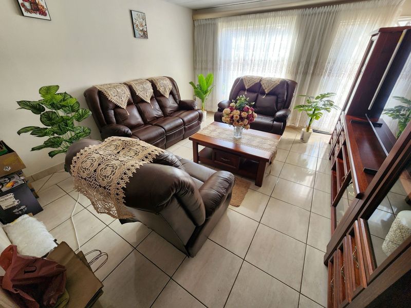 A bright living room featuring tiled flooring and large sliding glass doors with sheer curtains, providing ample natural light.