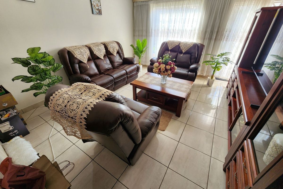 A bright living room featuring tiled flooring and large sliding glass doors with sheer curtains, providing ample natural light.