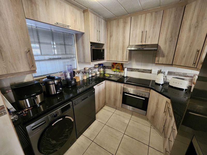 A functional kitchen featuring light wood-grain cabinetry, black granite countertops, built-in appliances, and tiled flooring with a window for natural light.