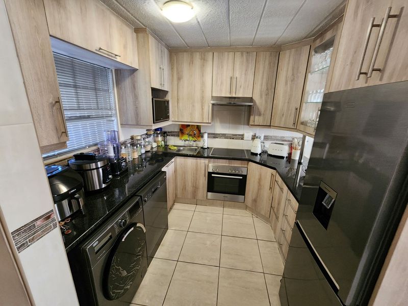 A functional kitchen featuring light wood-look cabinetry, granite countertops, built-in oven, electric hob, and integrated appliances with tiled flooring.