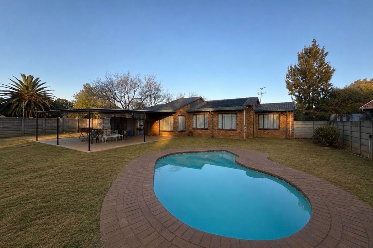 Rear view of a face brick house featuring a swimming pool with paved surround, a covered patio area, and roof-mounted solar panels.
