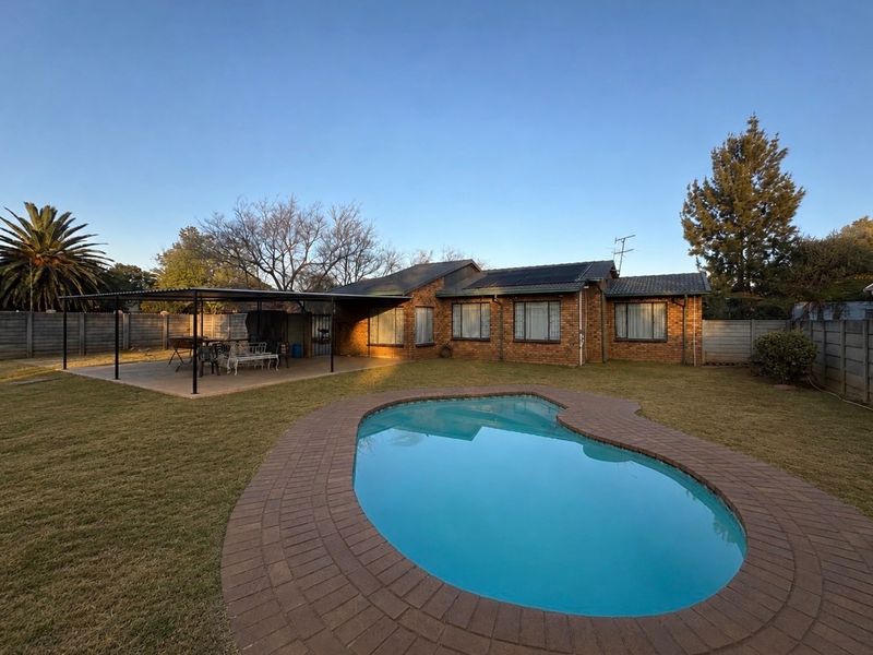 Rear view of a face brick house featuring a swimming pool with paved surround, a covered patio area, and roof-mounted solar panels.
