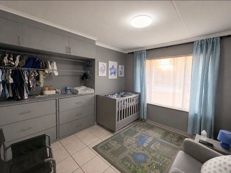 A well-maintained bedroom featuring neutral grey built-in cabinetry, tiled flooring, and large windows with curtains, providing a functional and organized living space.