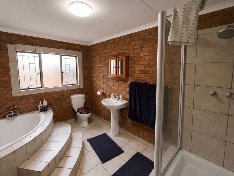 A spacious bathroom featuring exposed brick walls, a corner bathtub with tiled steps, a pedestal basin, and a separate glass-enclosed shower.