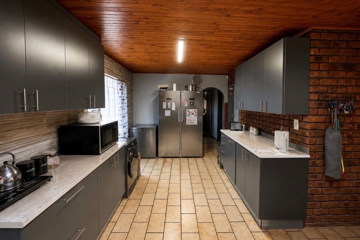 A functional kitchen featuring modern grey cabinetry, stone-look countertops, exposed brick accents, and a warm timber ceiling with tiled flooring.