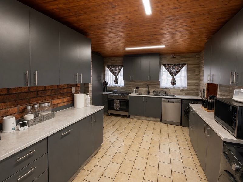 Modernized kitchen featuring dark grey cabinetry, laminate countertops, exposed brick accents, and a warm timber ceiling with tiled flooring.