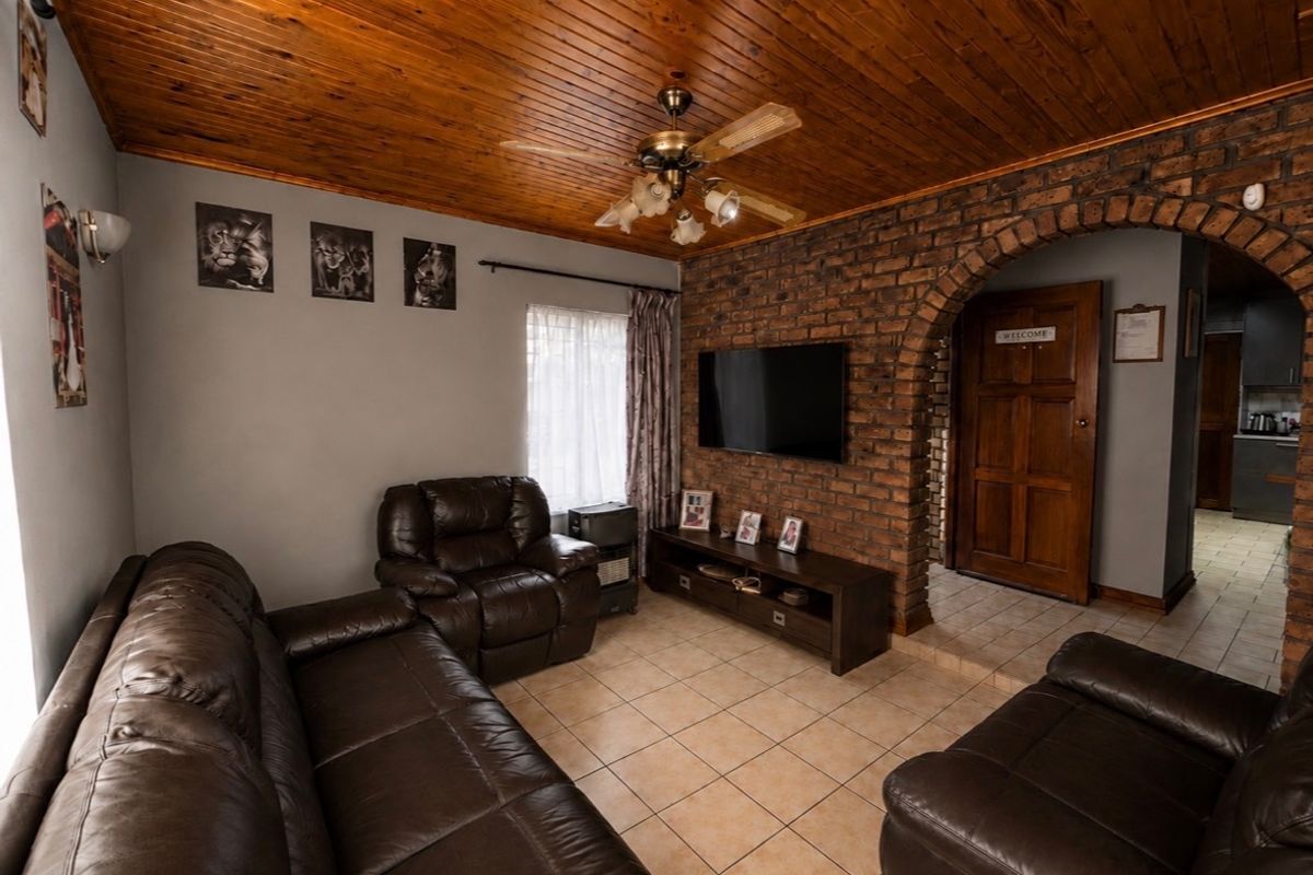 A cozy living room featuring a distinctive timber ceiling, exposed brick wall with an arched entrance, and neutral tiled flooring.