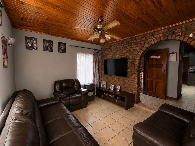 A cozy living room featuring a distinctive timber ceiling, exposed brick wall with an arched entrance, and neutral tiled flooring.
