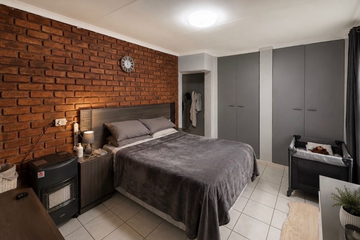 A well-maintained bedroom featuring an exposed brick accent wall, neutral tiled flooring, and ample built-in cupboard storage.