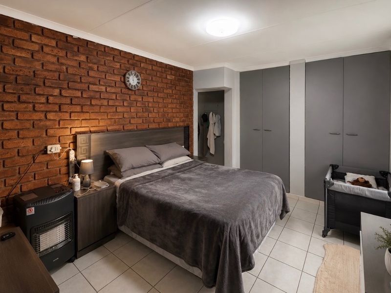 A well-maintained bedroom featuring an exposed brick accent wall, neutral tiled flooring, and ample built-in cupboard storage.