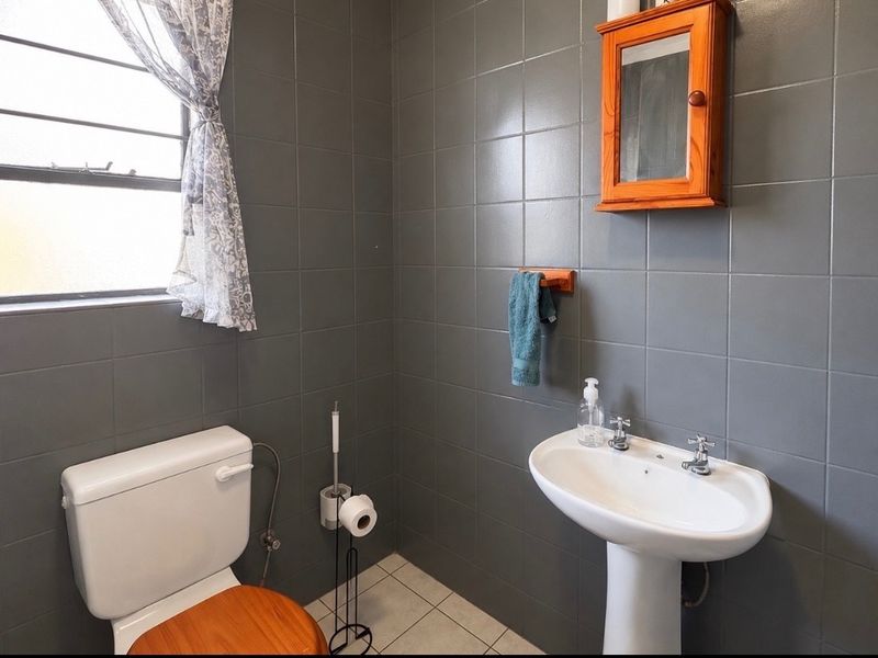A functional bathroom featuring dark grey wall tiling, a white pedestal washbasin, a standard toilet, and a wooden wall-mounted medicine cabinet.