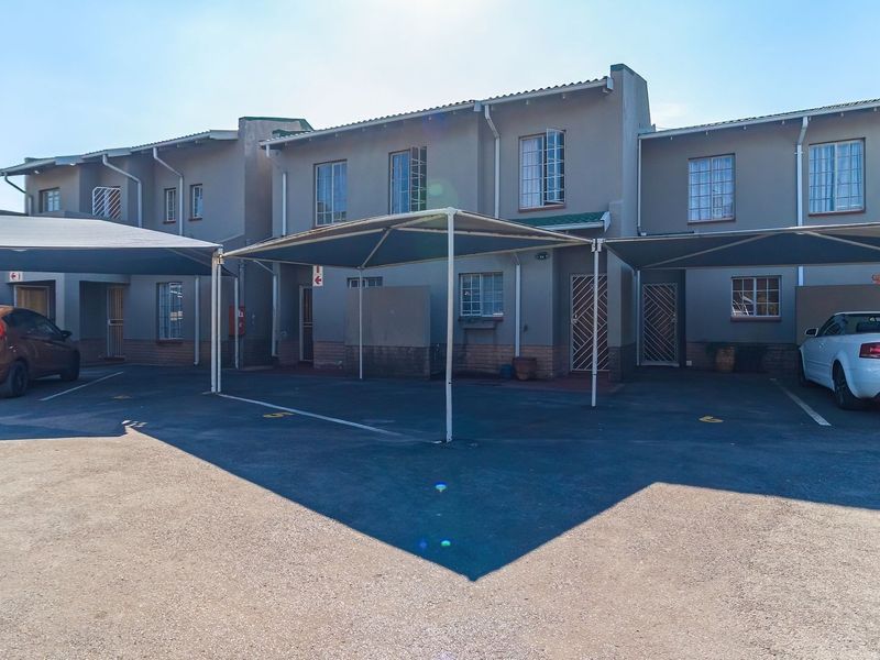 Front elevation of a townhouse complex featuring covered parking bays, paved driveway, and secure entrance points with security gates.