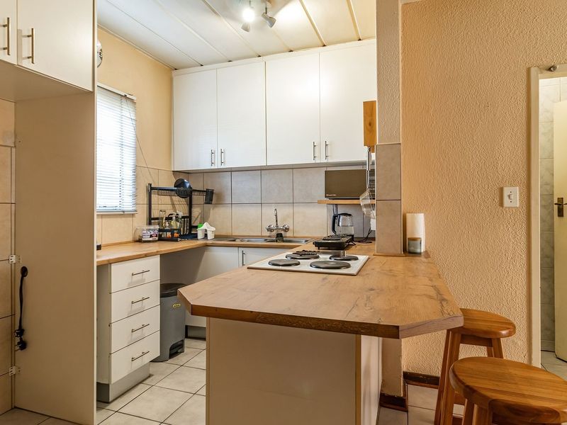 A functional kitchen featuring white cabinetry, a wood-look laminate countertop, an integrated electric hob, and tiled flooring with a breakfast bar area.