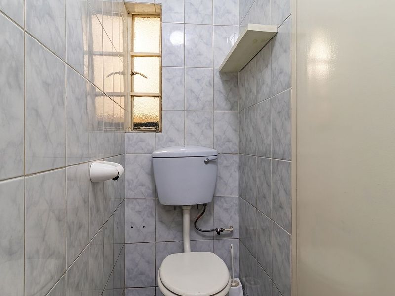 A compact, dated bathroom featuring full-height ceramic wall tiling, a standard toilet, and a small fixed shelf.
