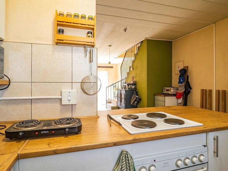 A functional kitchen area featuring wooden countertops, built-in cabinetry, and an electric hob, with an open-plan layout leading to a staircase.