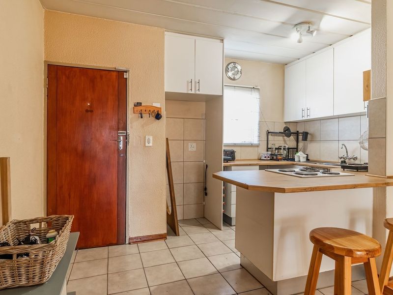 A functional kitchen featuring white cabinetry, a wooden breakfast bar, tiled flooring, and a built-in hob, offering a practical layout for daily use.