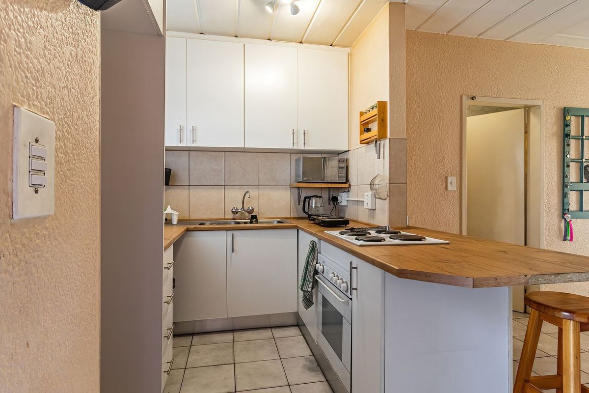 A functional kitchen featuring white cabinetry, a wood-look laminate countertop, built-in oven, electric hob, and tiled flooring.