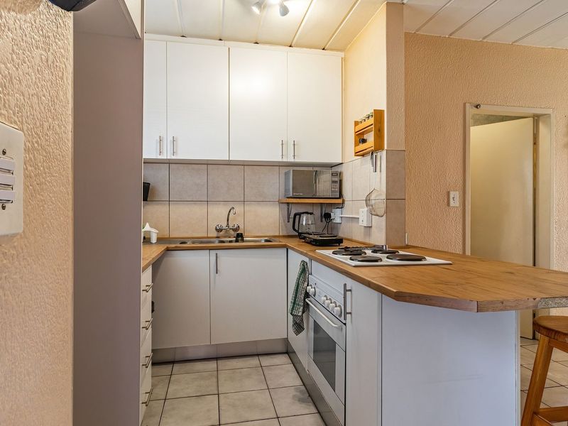 A functional kitchen featuring white cabinetry, a wood-look laminate countertop, built-in oven, electric hob, and tiled flooring.