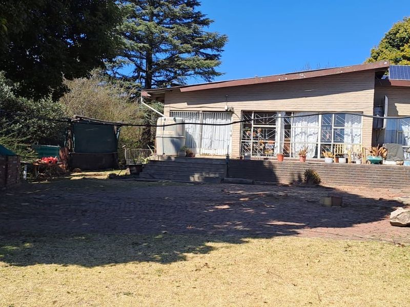 Rear view of the house featuring a brick paved patio, concrete steps, and roof-mounted solar panels set within a spacious garden area.