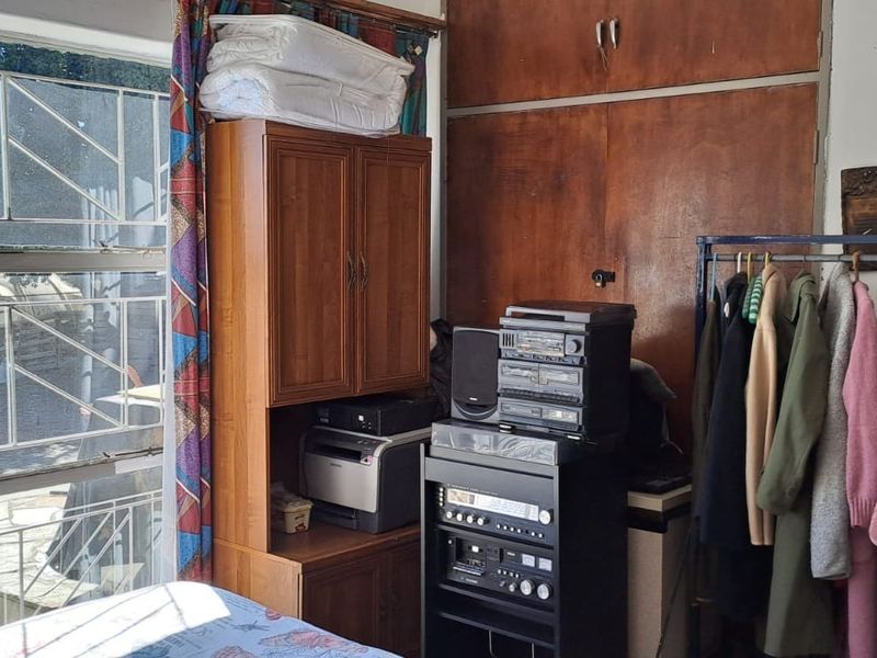 A bedroom featuring large metal-framed windows and built-in wooden cupboards, offering potential for modernization and improved storage solutions.