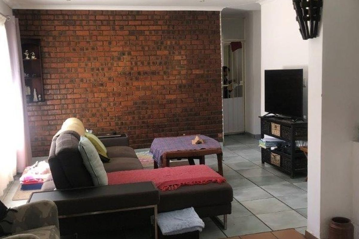 A living room featuring a prominent exposed brick feature wall, tiled flooring, and recessed lighting, offering a solid foundation for modern interior updates.