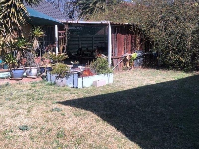 Rear garden area featuring a covered patio space, timber fencing, and a lawn, offering potential for landscaping and outdoor improvement.