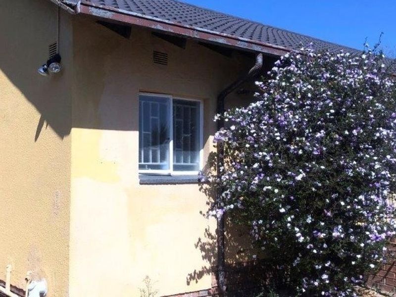 A view of the rear exterior wall of the house, featuring a tiled roof, security bars on windows, and weathered wall finishes.