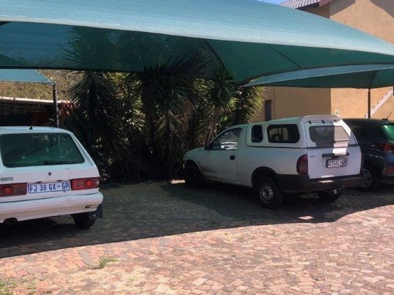 Outdoor parking area featuring a shade cloth carport structure and paved driveway surface.