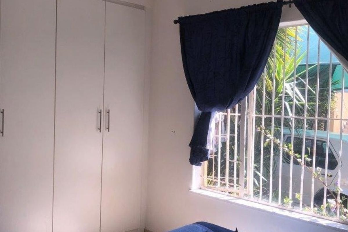 A bedroom featuring built-in cupboards and a window fitted with security bars, offering a functional and secure living space.
