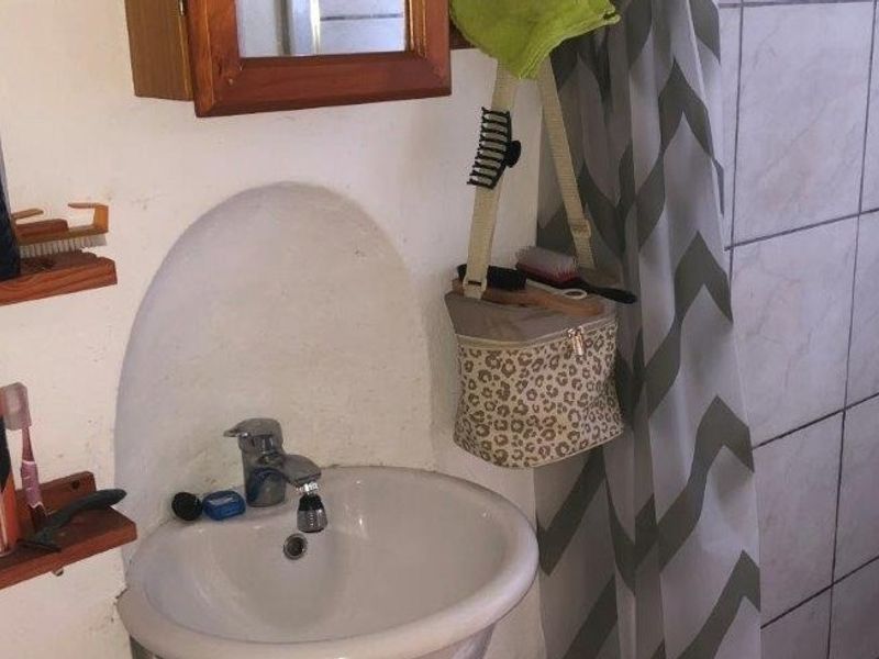 A compact bathroom featuring a wall-mounted basin with chrome mixer tap and a tiled shower enclosure with dated finishes.
