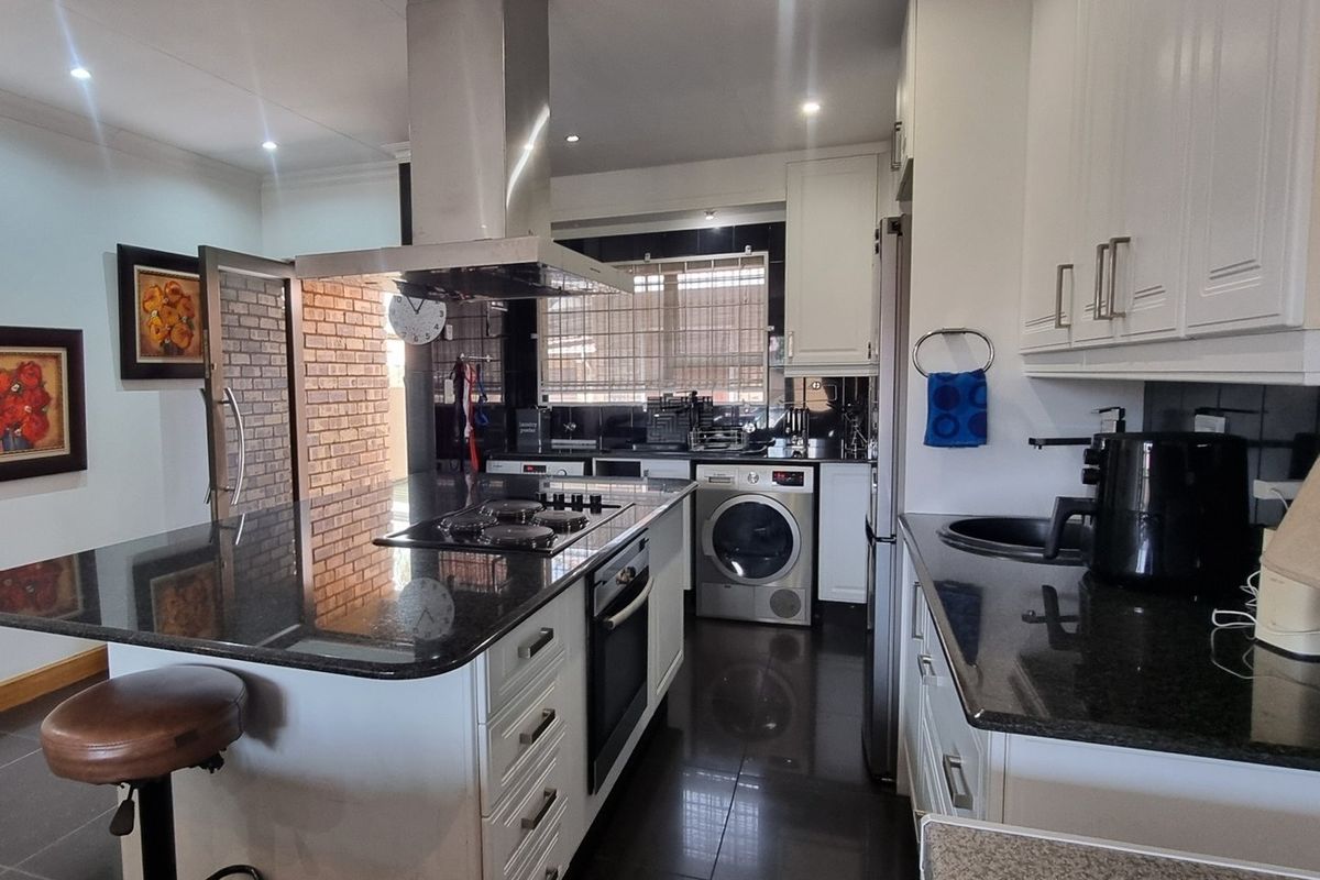 Modern kitchen featuring granite countertops, built-in oven, gas hob with extractor fan, and ample white cabinetry with dark tiled flooring.