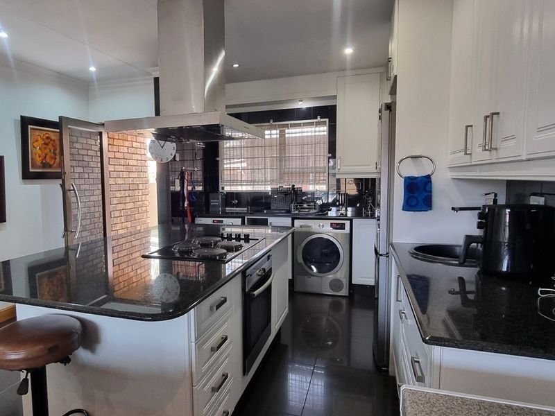 Modern kitchen featuring granite countertops, built-in oven, gas hob with extractor fan, and ample white cabinetry with dark tiled flooring.