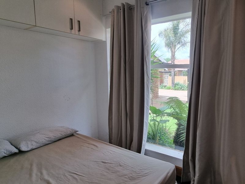 A bedroom featuring built-in overhead storage cabinetry and a large window providing natural light and garden views.