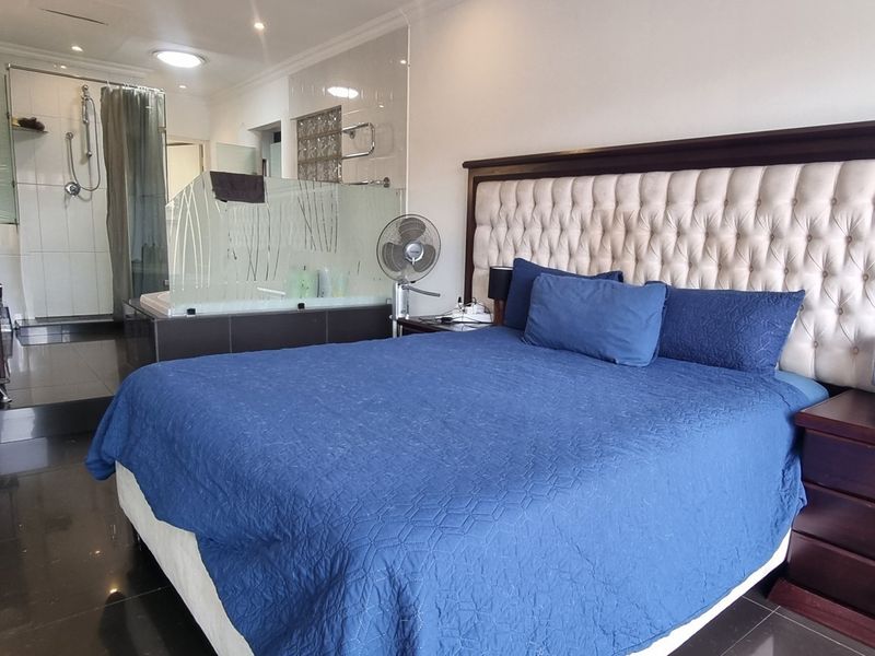 Spacious bedroom featuring an open-plan en-suite bathroom with a glass shower enclosure and built-in bathtub, finished with modern dark floor tiles.