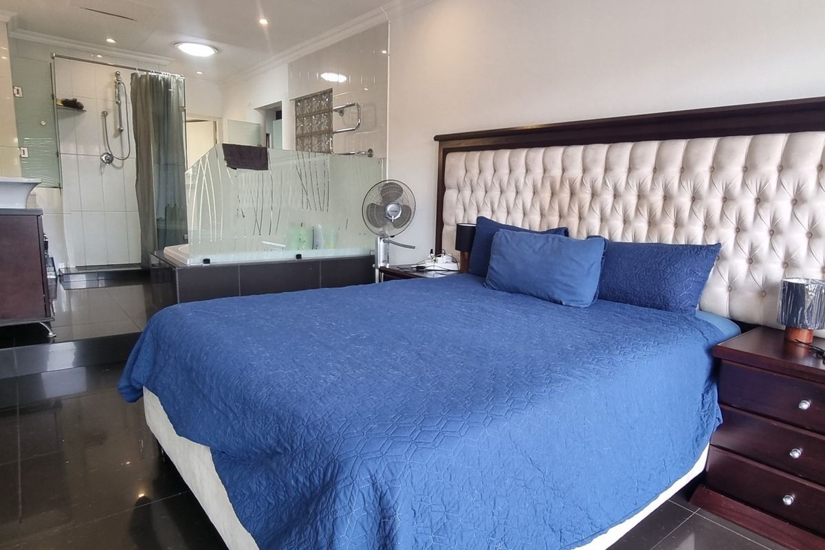 Spacious bedroom featuring an open-plan en-suite bathroom with a glass shower enclosure and built-in bathtub, finished with modern dark floor tiles.