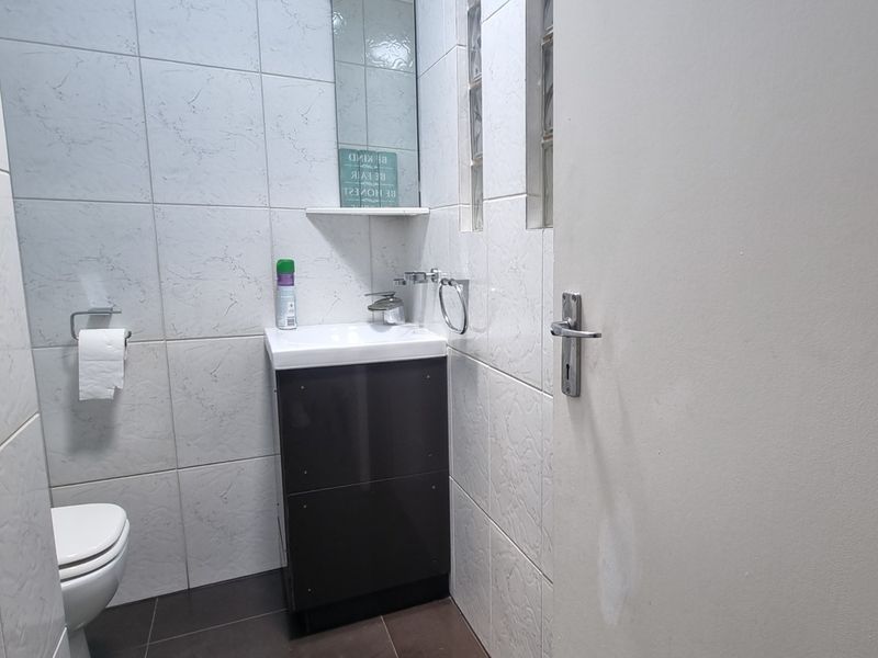 A compact guest bathroom featuring a modern vanity cabinet, basin, toilet, and tiled finishes with a glass block window for natural light.