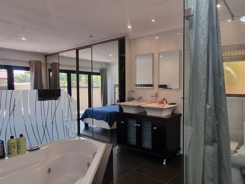 Modern en-suite bathroom featuring a double vanity, corner bathtub, glass shower enclosure, and extensive built-in mirrored cabinetry, seamlessly integrated with the bedroom area.