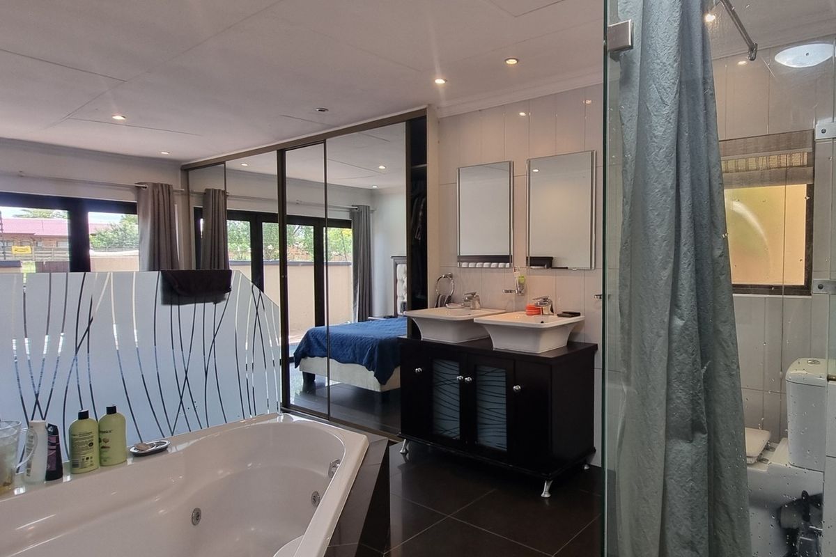 Modern en-suite bathroom featuring a double vanity, corner bathtub, glass shower enclosure, and extensive built-in mirrored cabinetry, seamlessly integrated with the bedroom area.