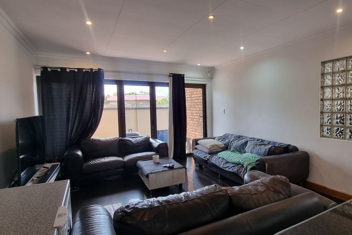 Spacious living room featuring tiled flooring, recessed downlighting, and a unique glass block feature wall, with direct access to the outdoor area.