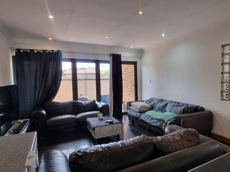 Spacious living room featuring tiled flooring, recessed downlighting, and a unique glass block feature wall, with direct access to the outdoor area.