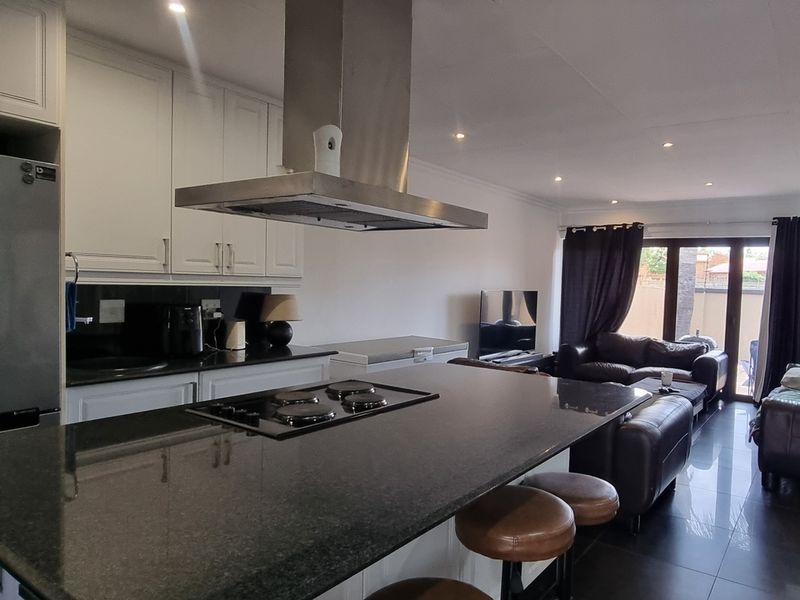 Spacious open-plan living area featuring a modern kitchen with a granite-topped island, built-in hob, extractor fan, and seamless flow to the outdoor patio area.