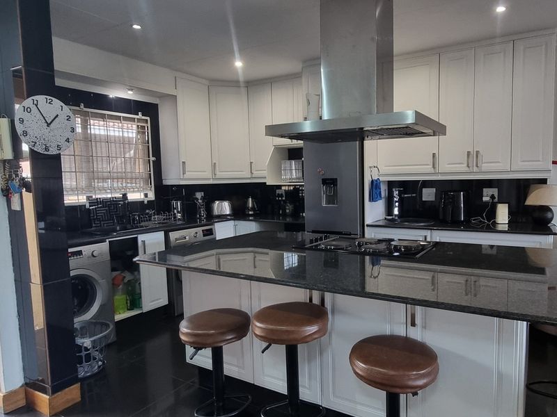A well-appointed kitchen featuring white cabinetry, dark granite countertops, a central island with a gas hob, and an integrated extractor fan.