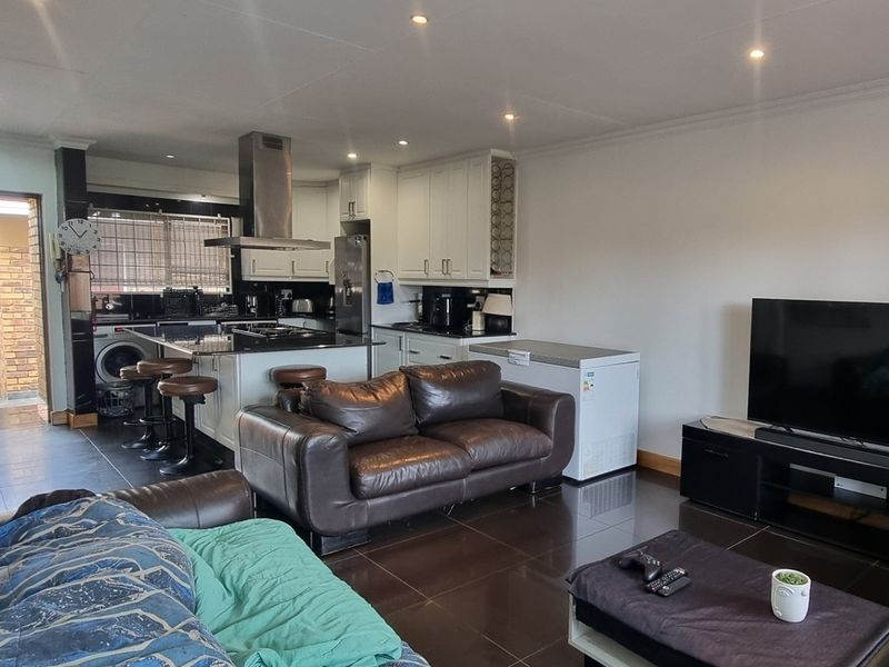 Spacious open-plan living area featuring a modern kitchen with a central island, dark tiled flooring, and recessed lighting, seamlessly connecting to the living space.