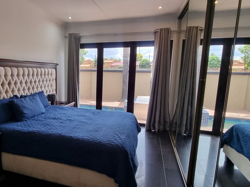 Spacious bedroom featuring tiled flooring, built-in cupboards with mirrored doors, and large sliding glass doors providing direct access to the pool area.